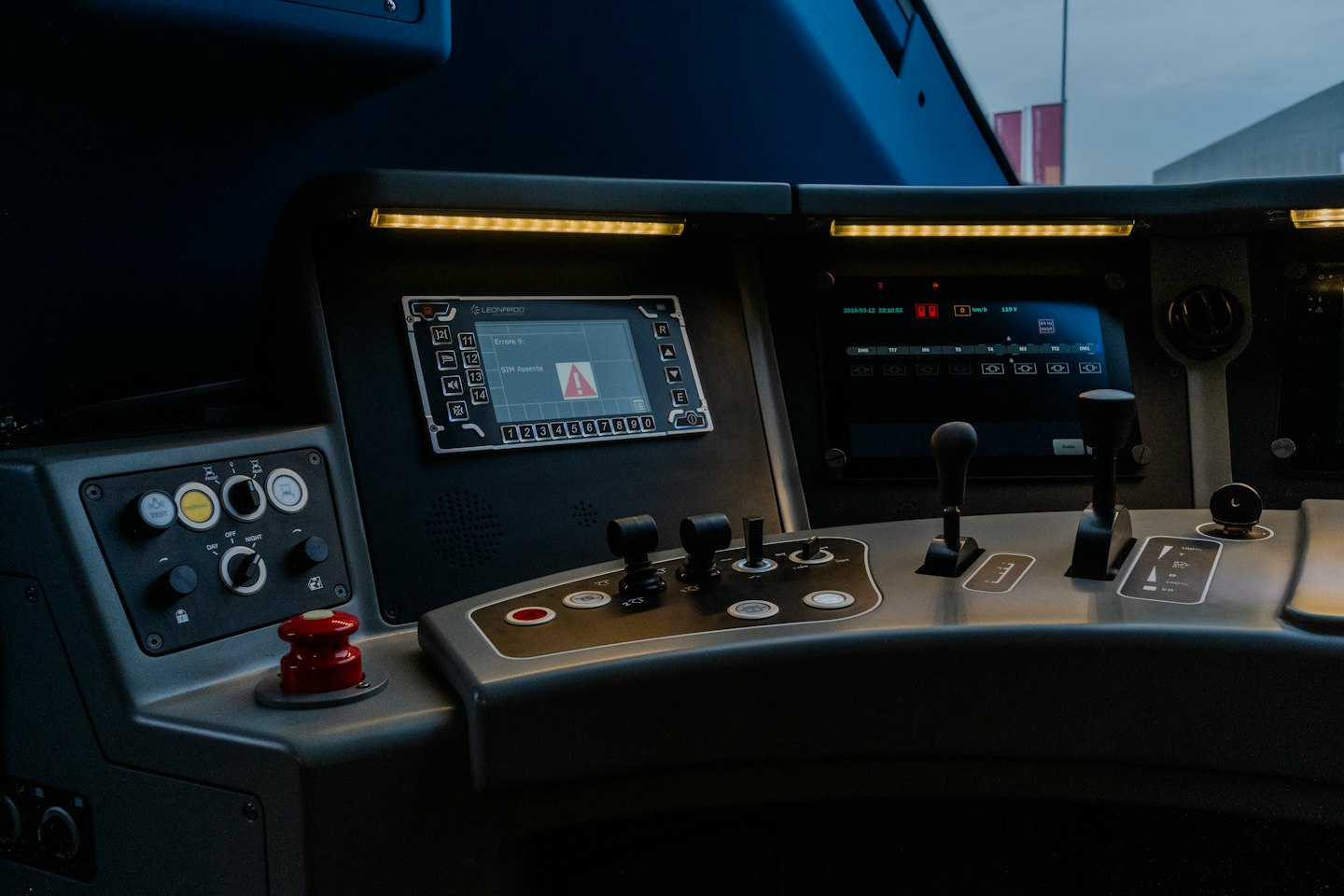 Train cockpit control panel with digital screens and emergency button.